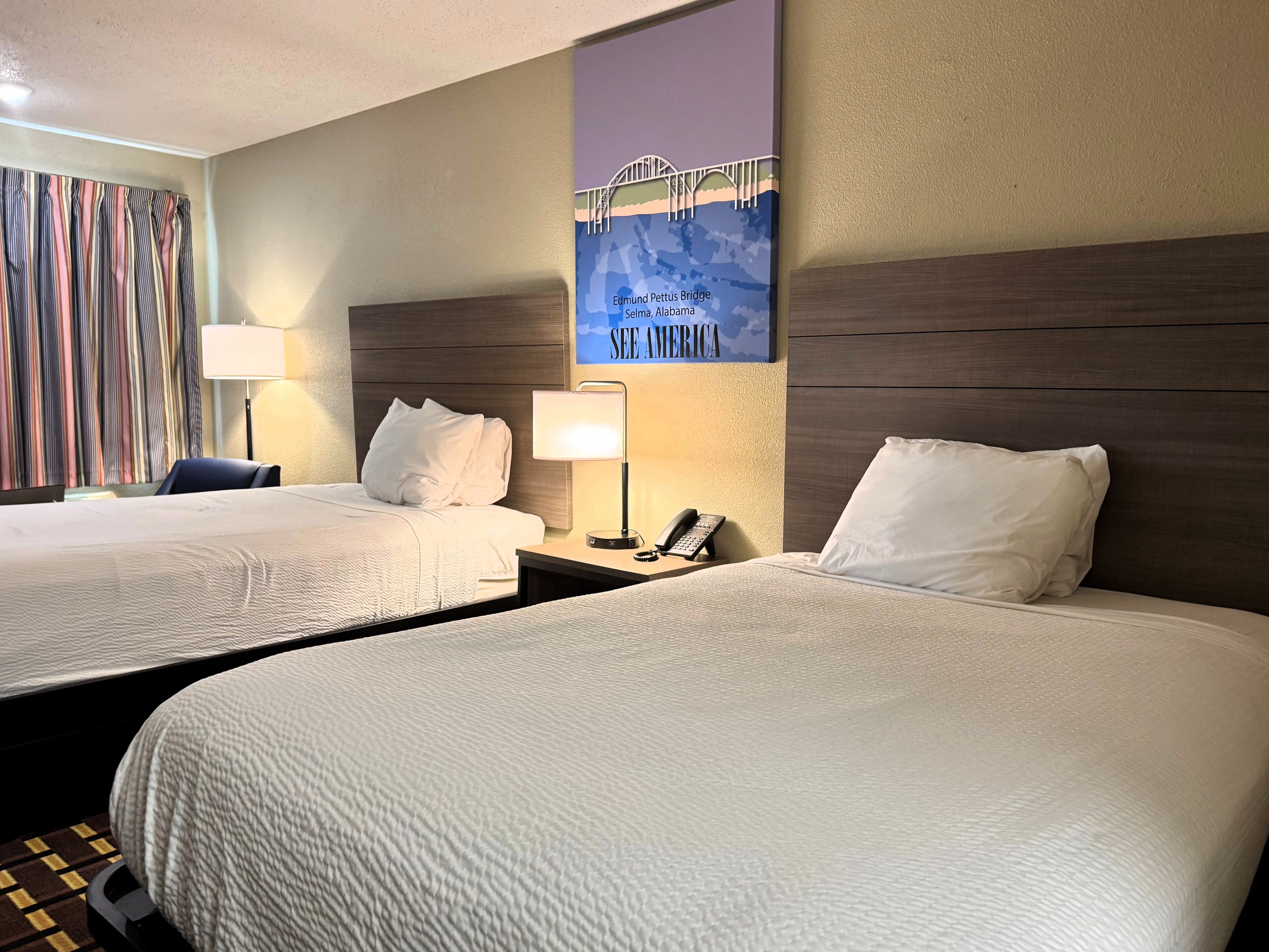 Ein Hotelzimmer mit zwei Betten, einem Nachttisch mit Lampe und Telefon sowie einer Wand mit einem Poster der Edmund Pettus Bridge.