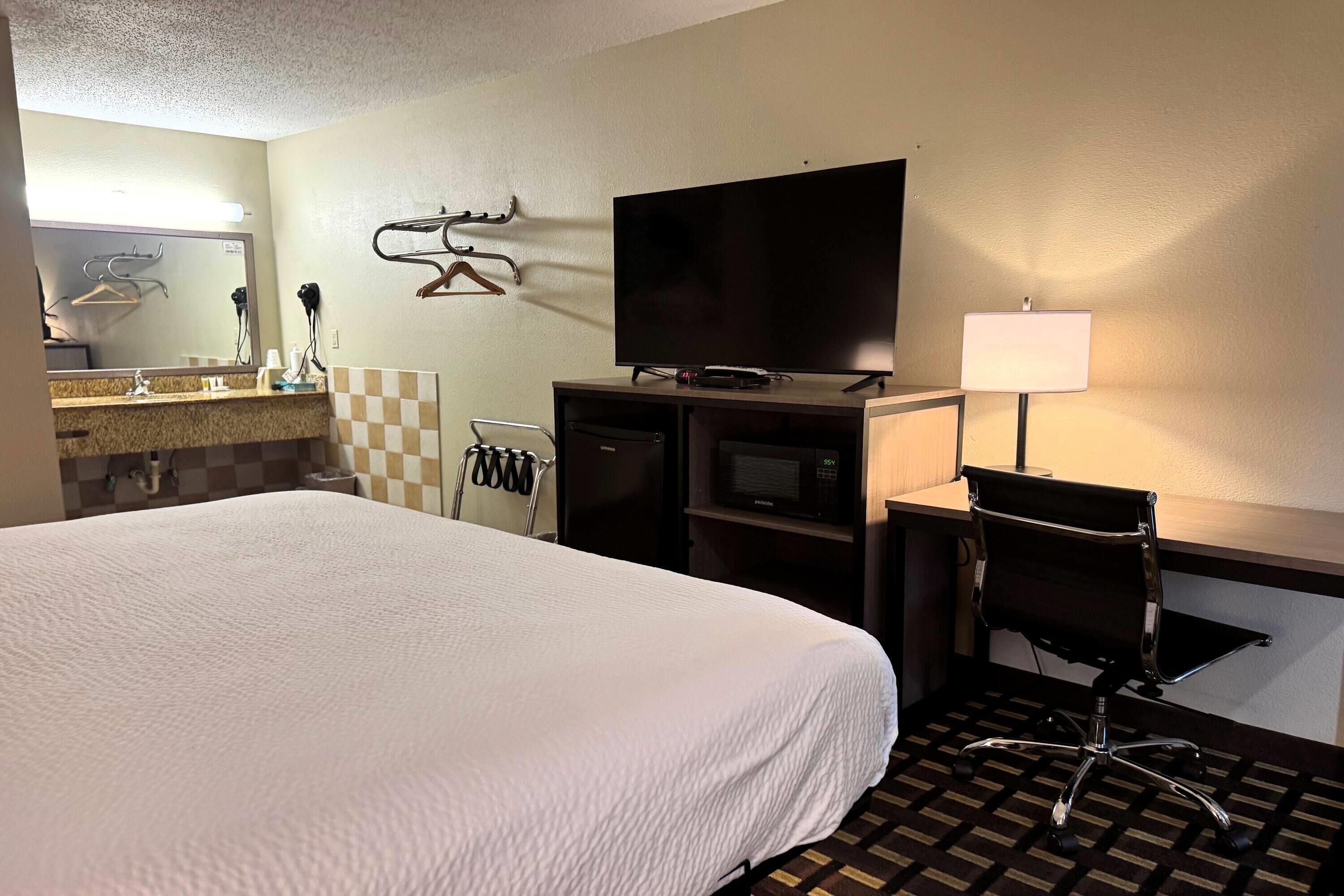 A hotel room with a large bed, a flat-screen TV, a desk with a chair, a lamp, and a microwave.