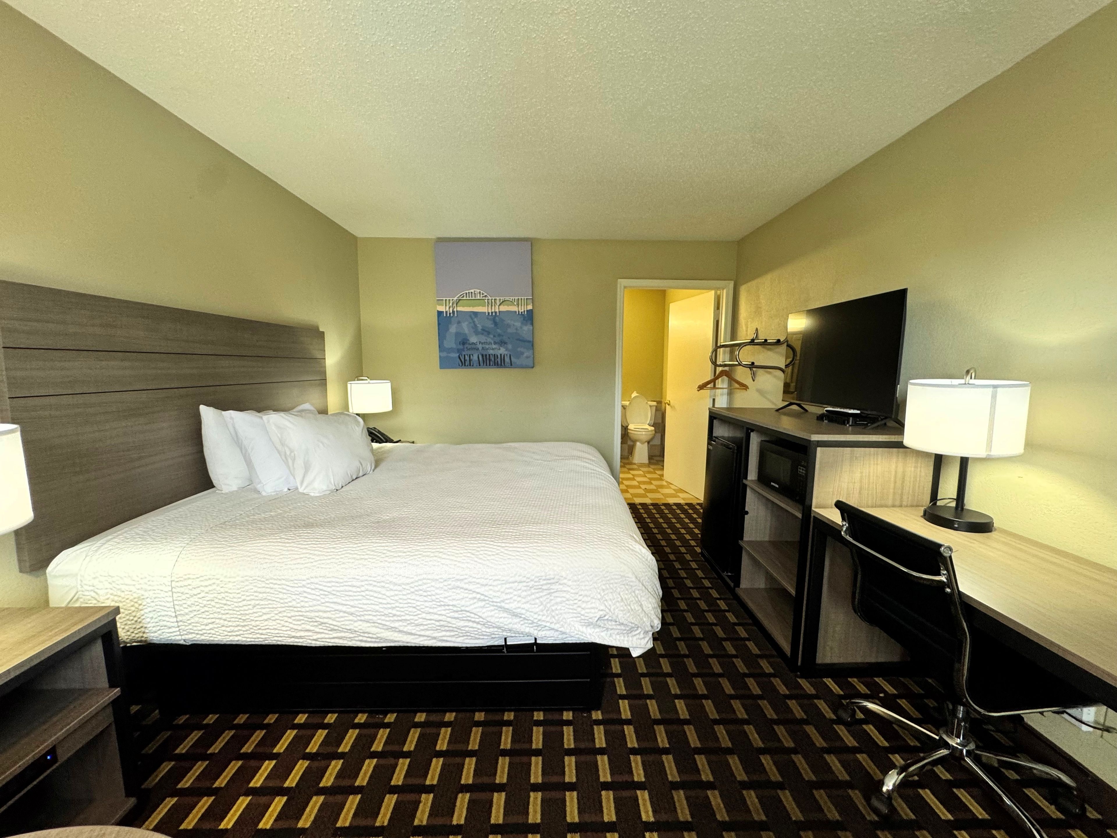 Une chambre d’hôtel comprenant un lit, des tables de chevet, un bureau avec une chaise, une télévision et une salle de bain visible à travers une porte ouverte.