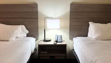 A hotel room with two beds, a nightstand with a lamp, a phone, and a small drawer.