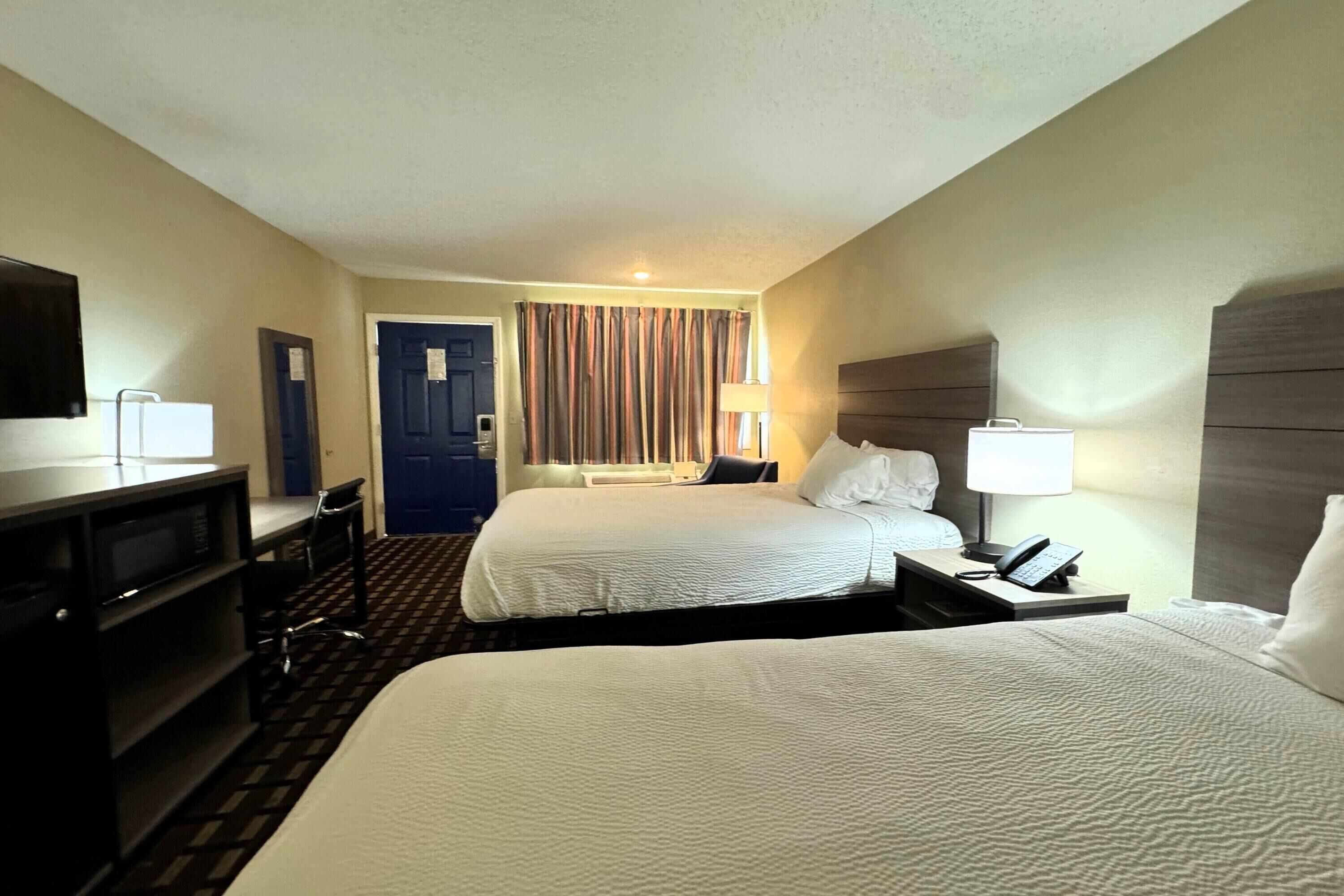 A hotel room with two beds, a desk, a TV, and a door.