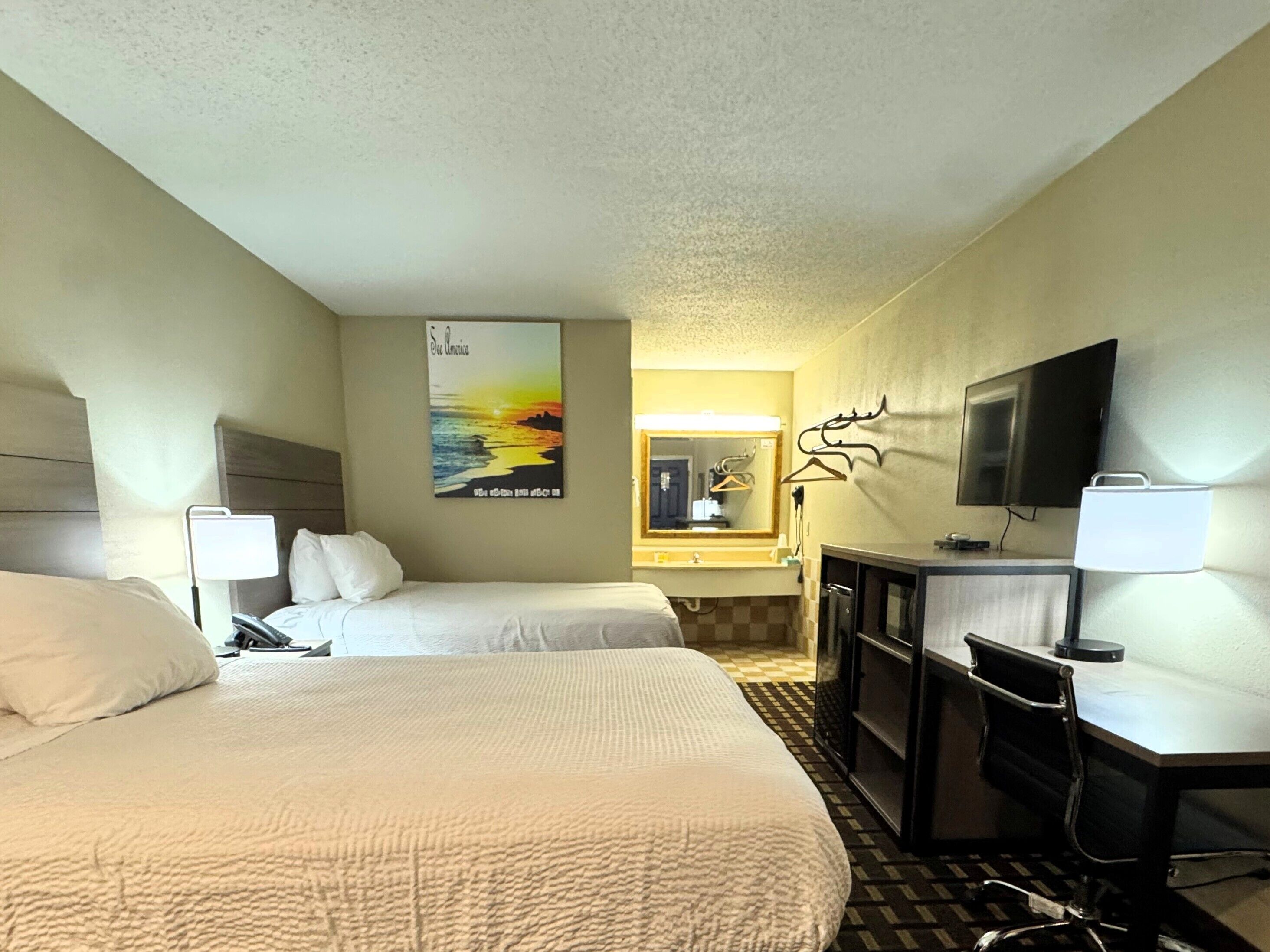 A hotel room with two beds, a desk, a TV, a mirror, and a poster on the wall.