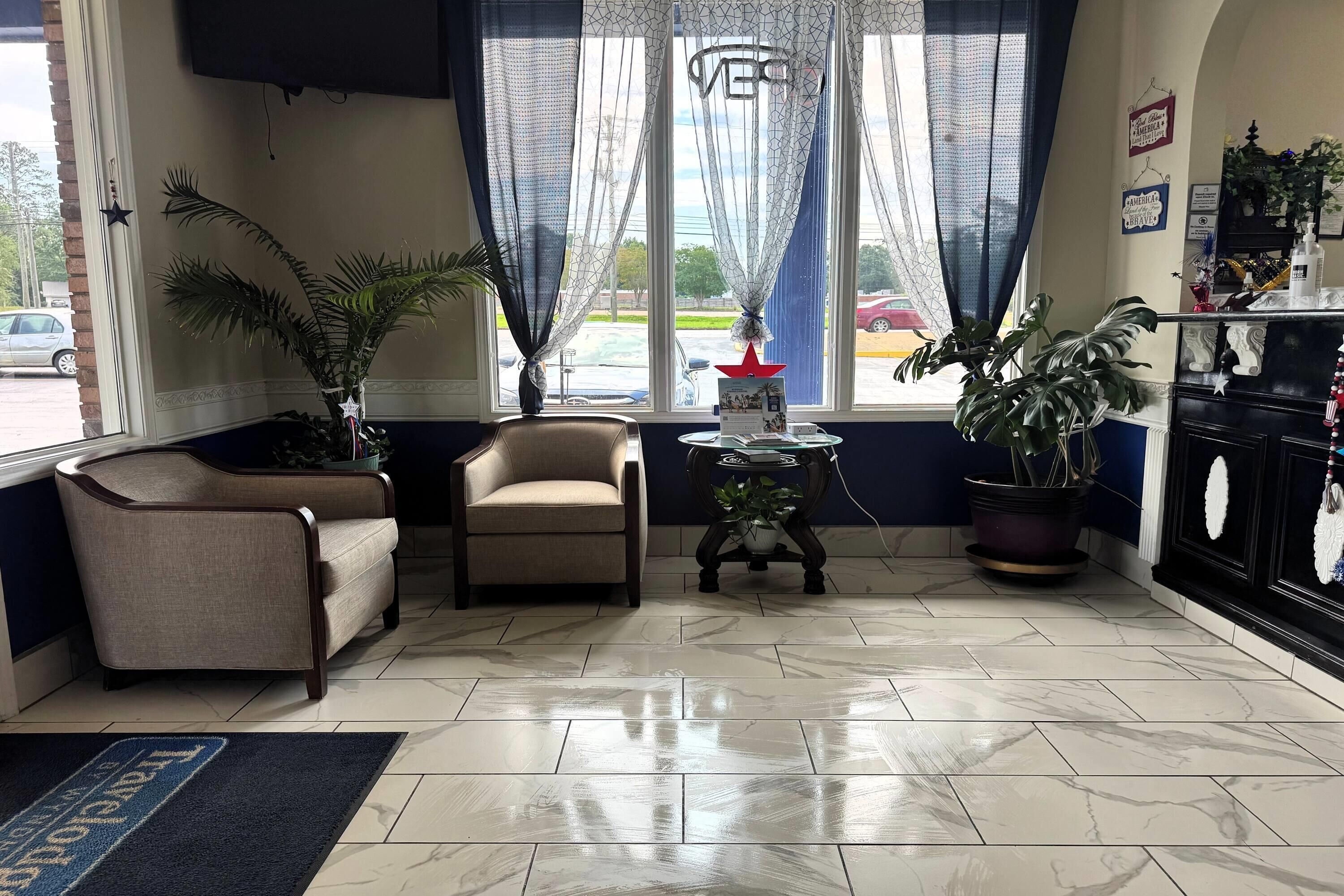 Una habitación con sofá, sillón, plantas en macetas, una mesita y vistas a través de una ventana.