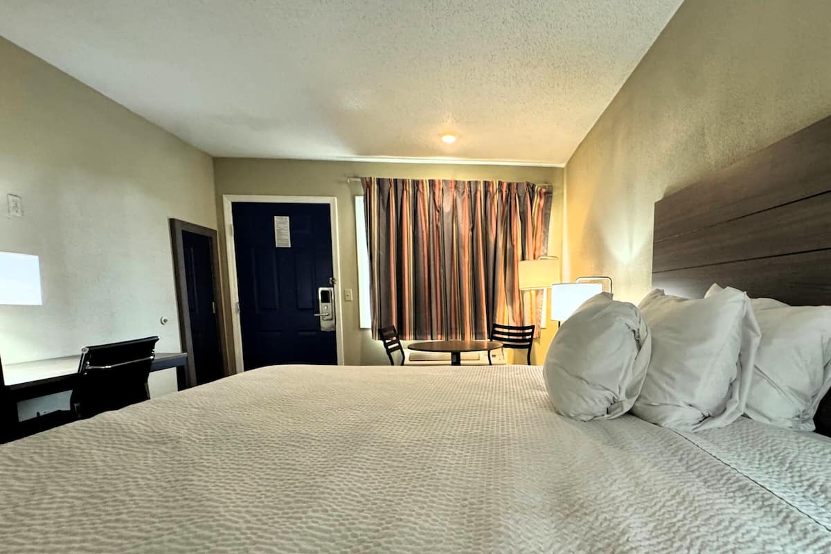 A hotel room with a large bed, a desk, a chair, a table, and a curtain.