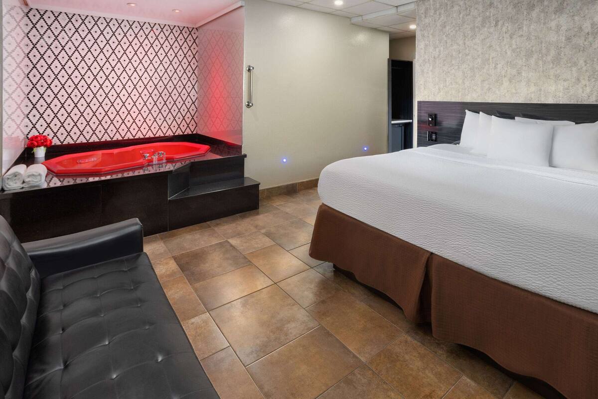 A hotel room with a large bed, a red jacuzzi, a black leather sofa, and a patterned wall.