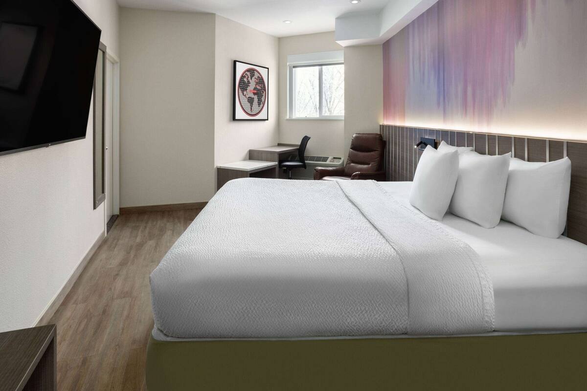 A modern hotel room with a large bed, a desk, a chair, and a TV.
