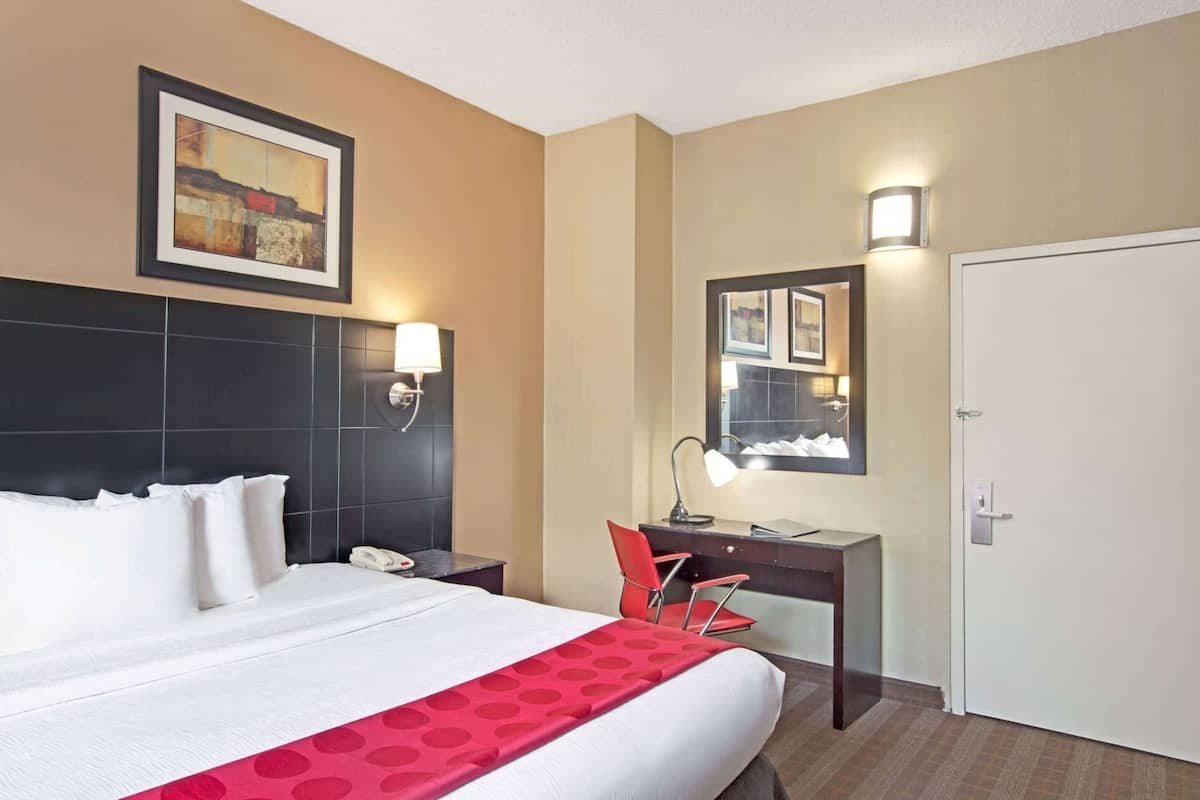 A hotel room with a bed, a desk, a chair, a telephone, a mirror, and a door.
