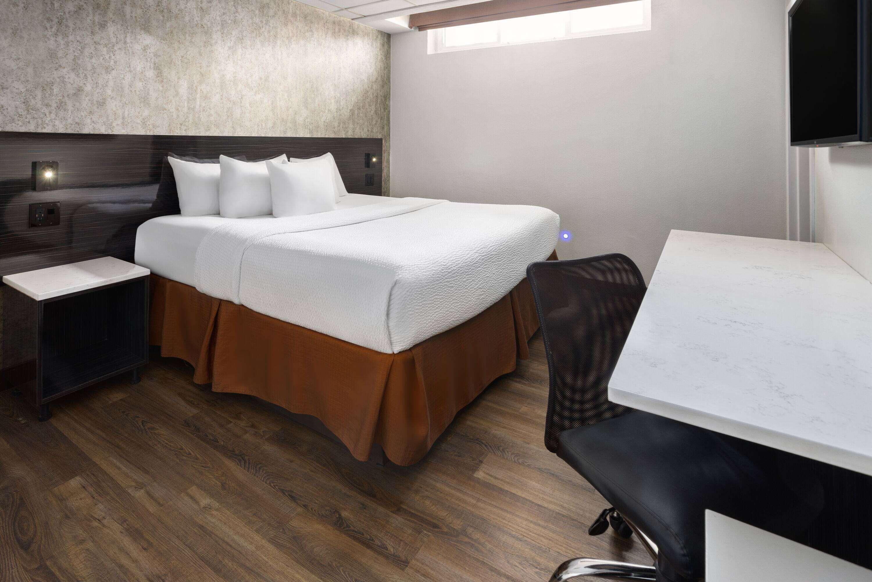 A modern hotel room with a large bed, a desk, and a TV.