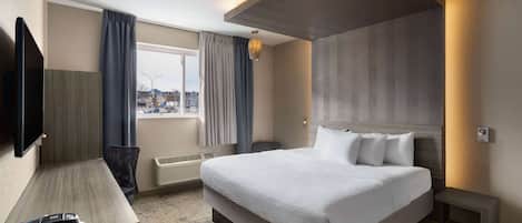 Habitación de hotel moderna con una cama grande, un escritorio, un televisor de pantalla plana y vistas a la ciudad.