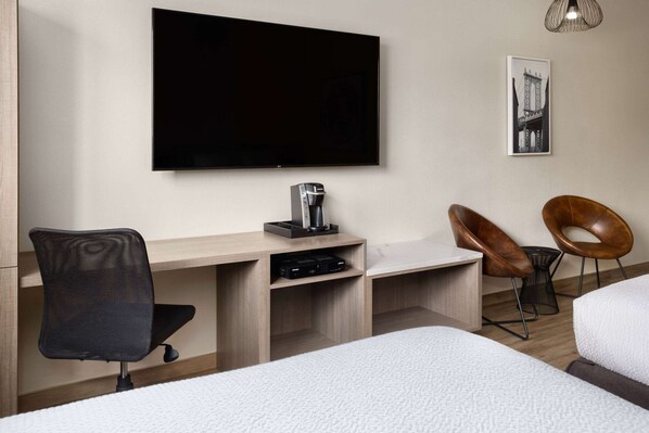 A hotel room with a flat-screen TV, a desk with a chair, a bed, and two chairs. - Ramada by Wyndham Bronx (Bronx)
