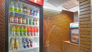 Un refrigerador lleno de diversas bebidas, un jarrón decorativo con plantas secas y una pequeña vitrina refrigerada en una habitación con paneles de madera.