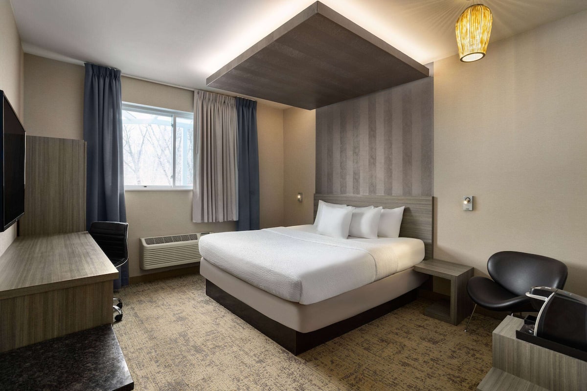 A modern hotel room with a large bed, a desk, a chair, and a TV.