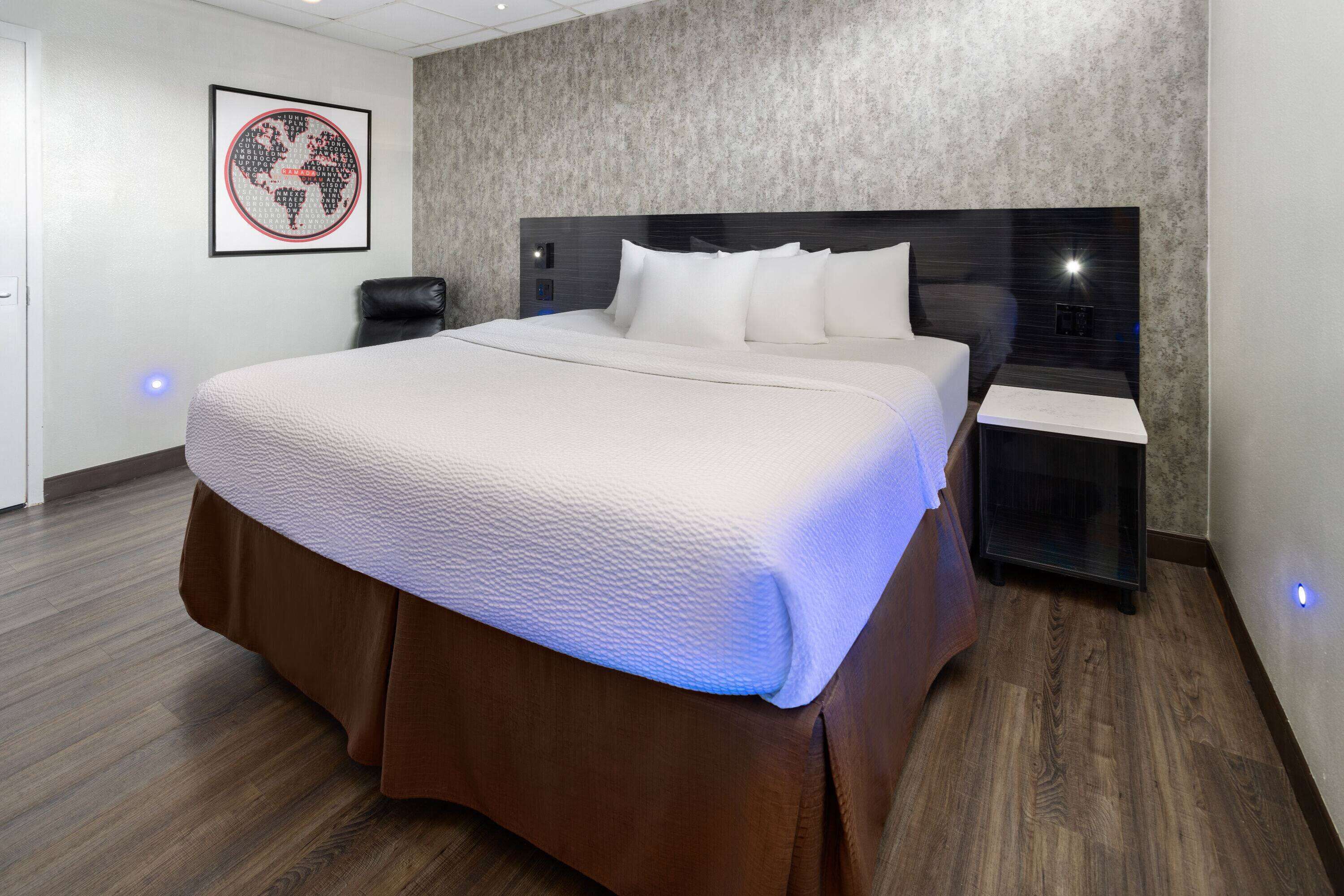Une chambre d’hôtel moderne dotée d’un grand lit, d’une tête de lit avec éclairage intégré, d’une table de chevet et d’une œuvre d’art accrochée au mur.