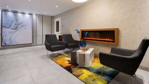 Un vestíbulo moderno con dos sillas negras, una alfombra colorida, una chimenea y un cuadro abstracto grande en la pared.