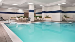 A large indoor swimming pool with clear blue water, surrounded by white and blue walls, and furnished with several chairs and tables. - Embassy Suites by Hilton Columbus Dublin (Dublin)