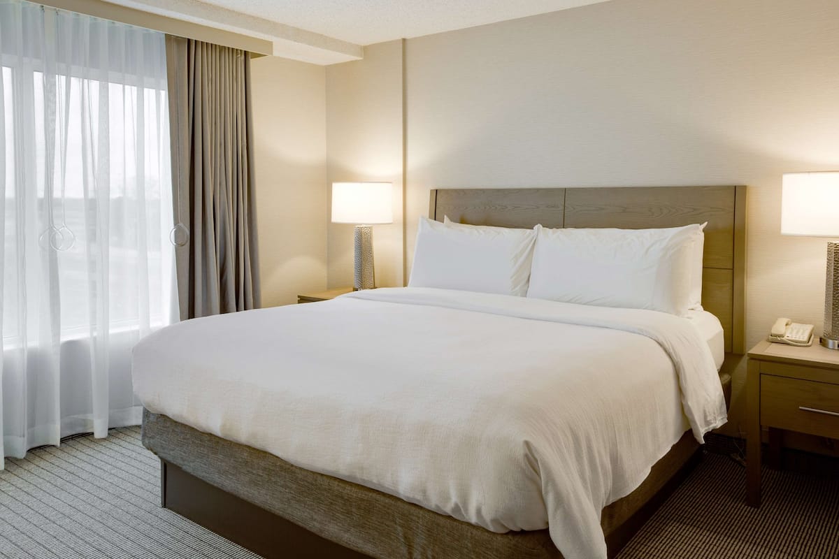 A hotel room with a large bed, a bedside table with a lamp, and a window with curtains.
