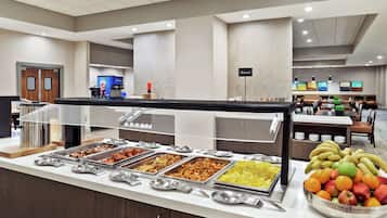 Un área de bufé con diversas opciones de comida, un espacio de comedor con mesas y sillas, y una máquina de café.