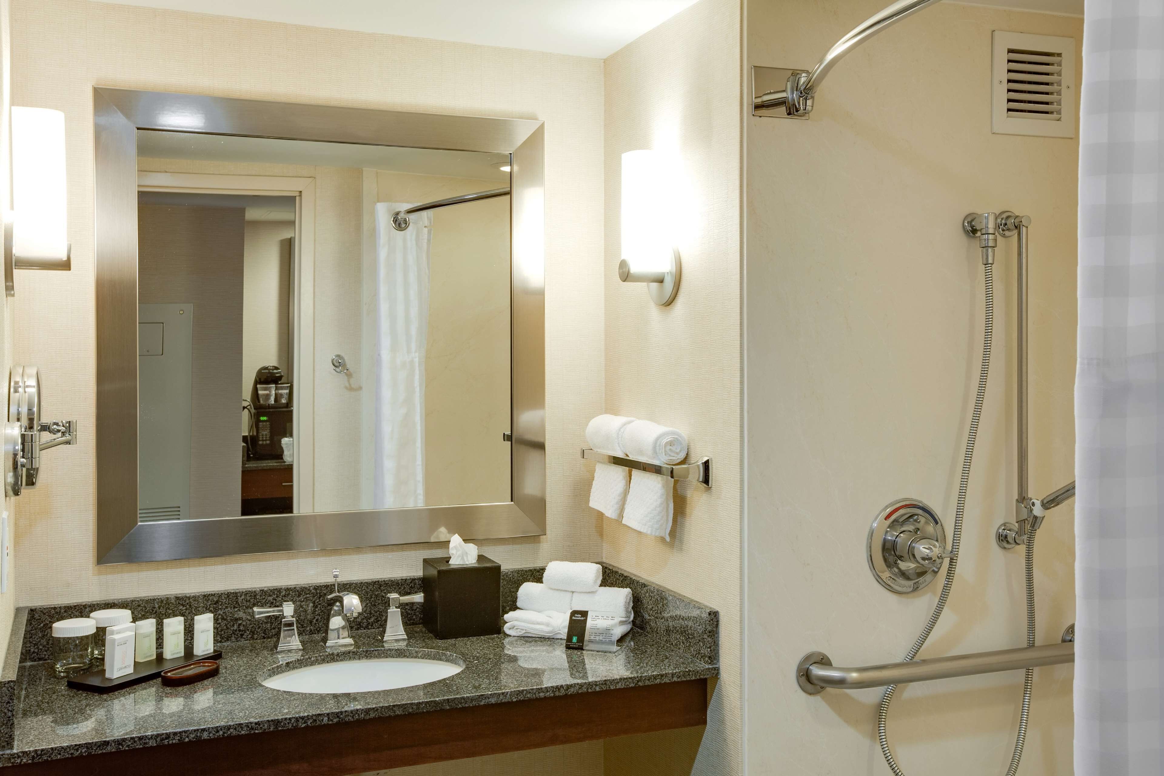 A hotel bathroom with a sink, mirror, towel rack, shower, and a hand dryer.