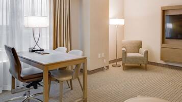 A hotel room with a wooden desk, two chairs, a TV, and a lamp.