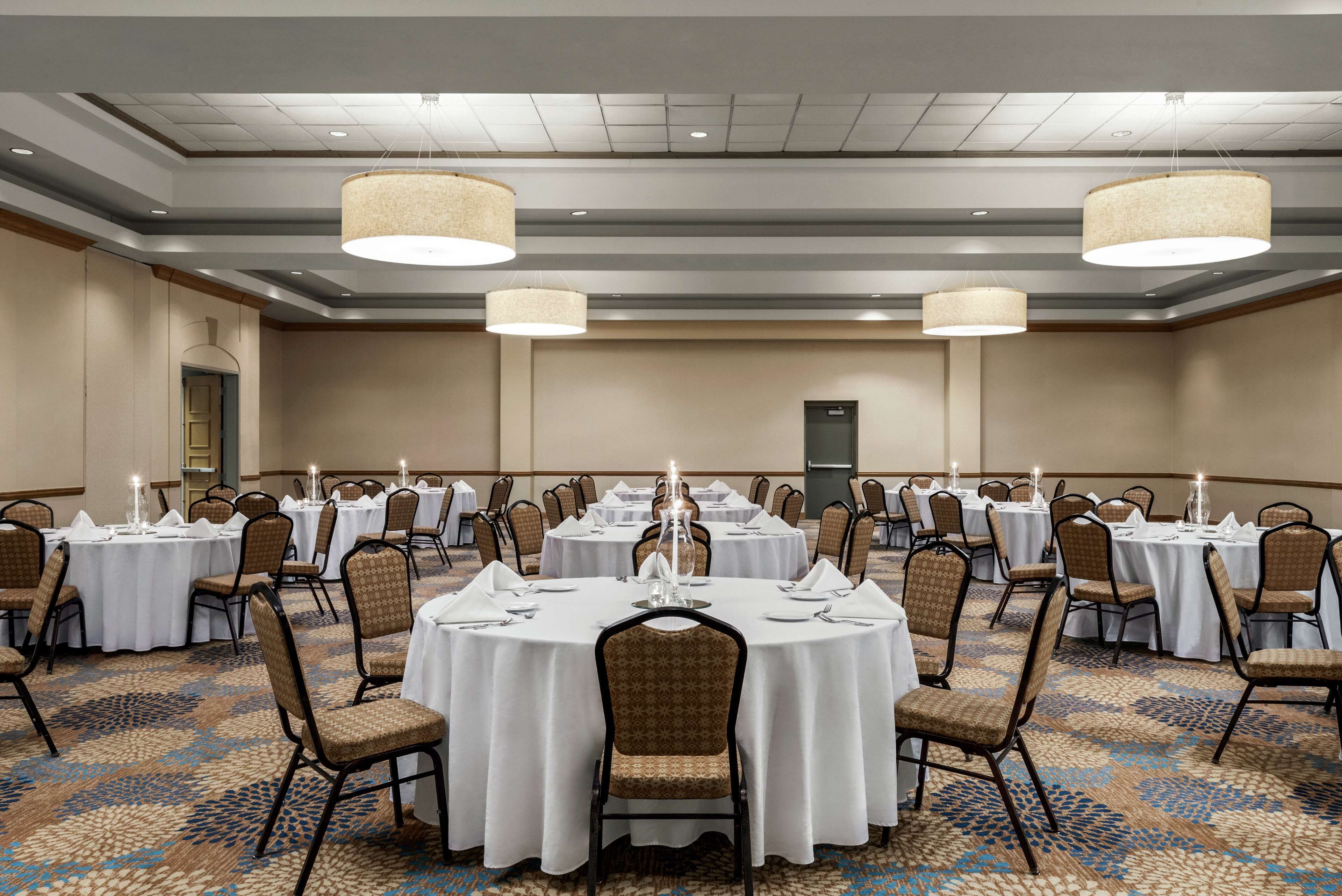 A banquet hall with round tables, chairs, and hanging chandeliers.