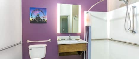 A bathroom with a purple wall, a white toilet, a sink with a mirror, and a shower with grab bars.