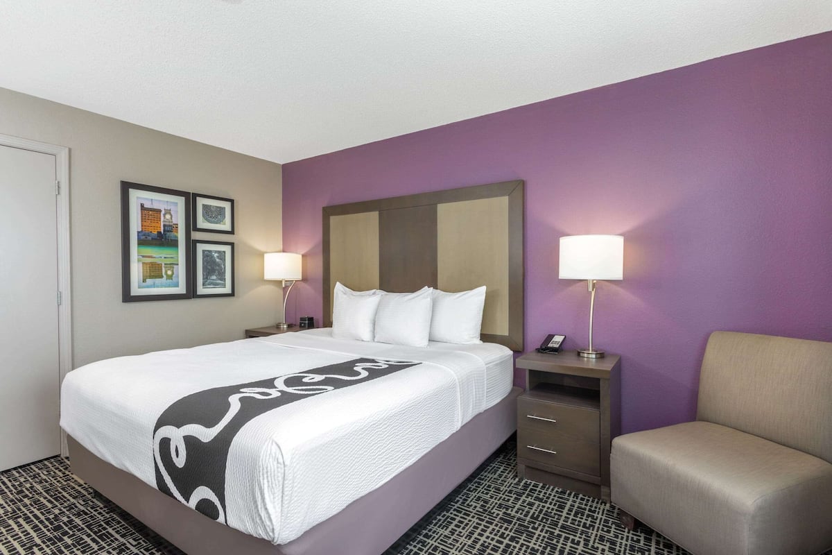 A hotel room with a bed, bedside tables, a chair, and wall art.