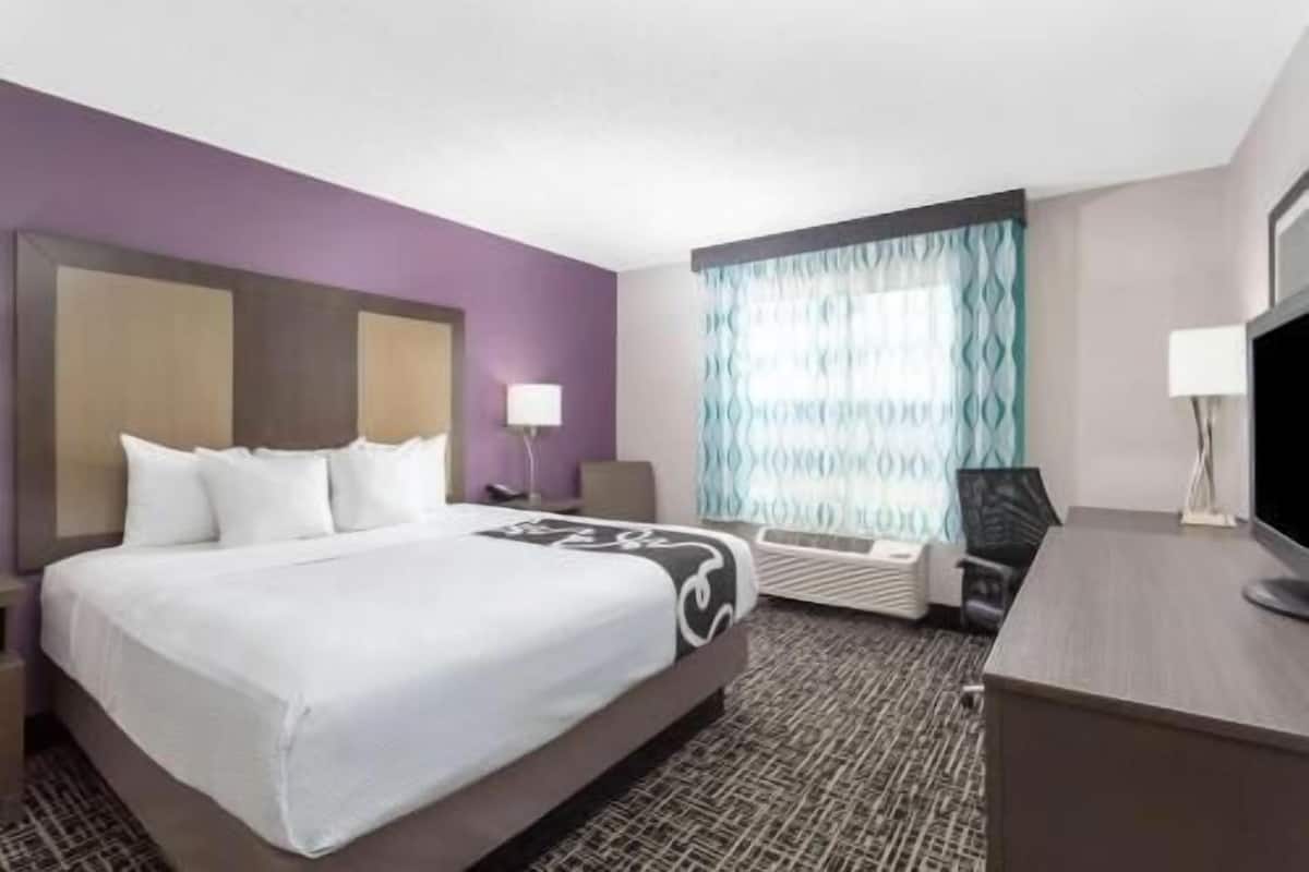 A hotel room with a bed, a desk, a chair, a lamp, and a television.
