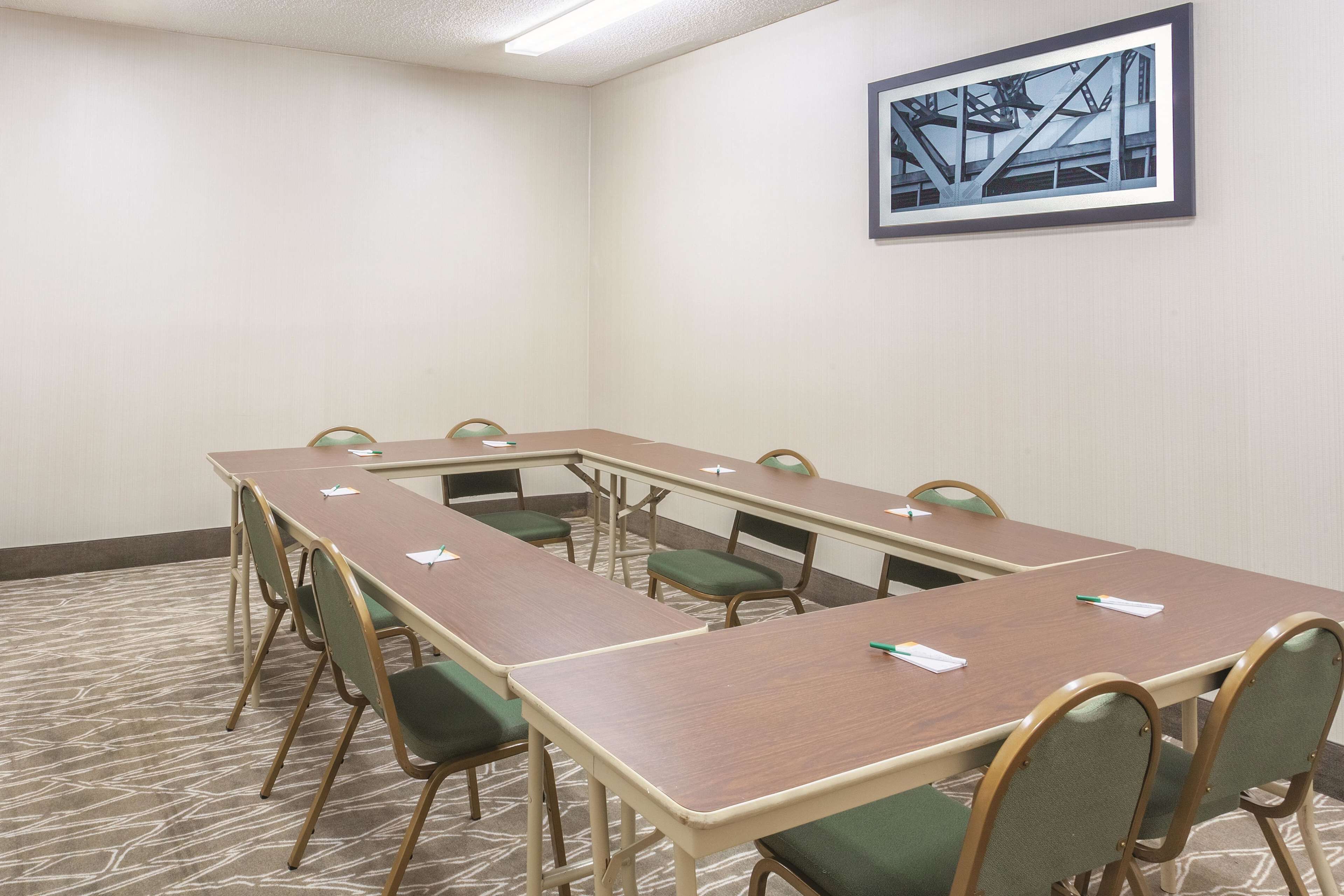 A conference room with a long table, green chairs, and a framed picture on the wall.