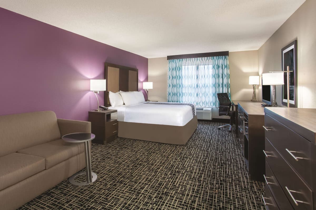 A hotel room with a bed, a sofa, a desk, and a dresser.