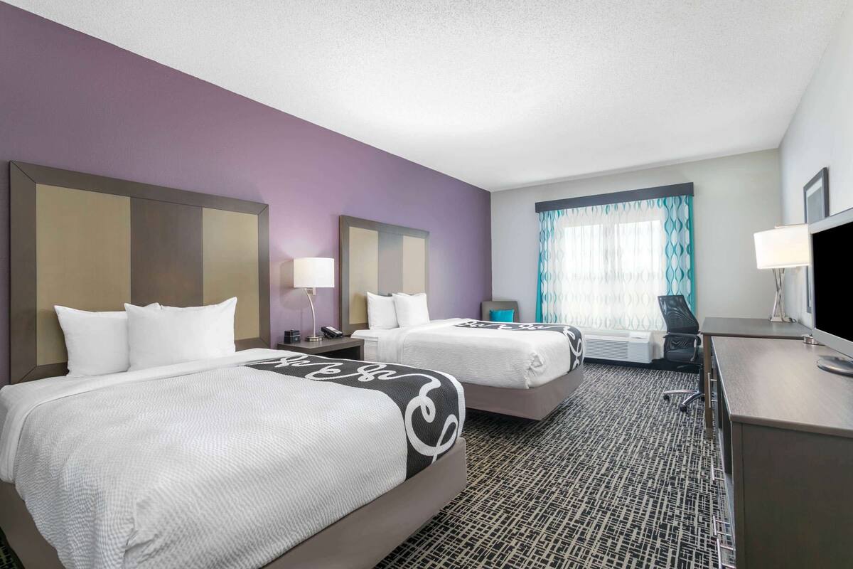 A hotel room with two beds, a desk, a chair, a TV, and a window with curtains.