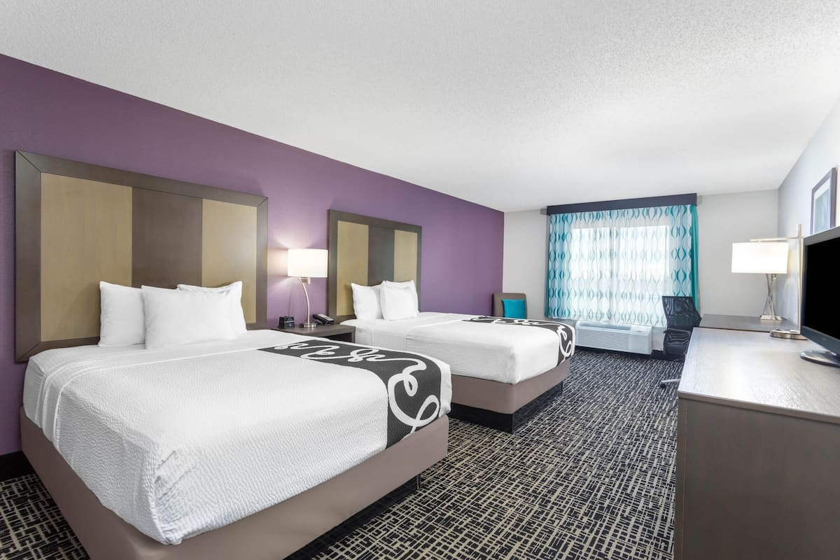 A hotel room with two beds, a desk, a TV, and a window with curtains.