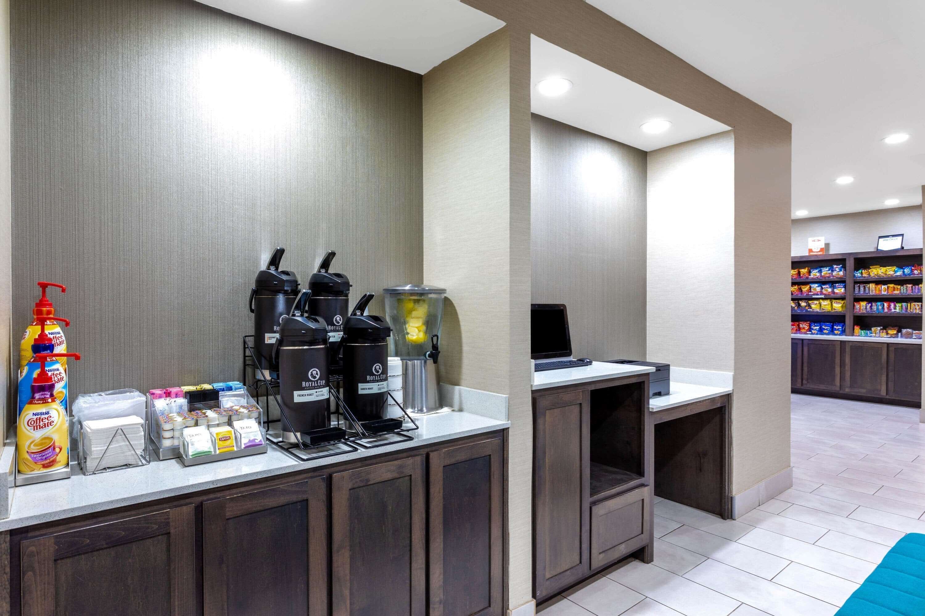 A hotel reception area with a coffee station, self-service beverage dispensers, and a snack bar in the background.