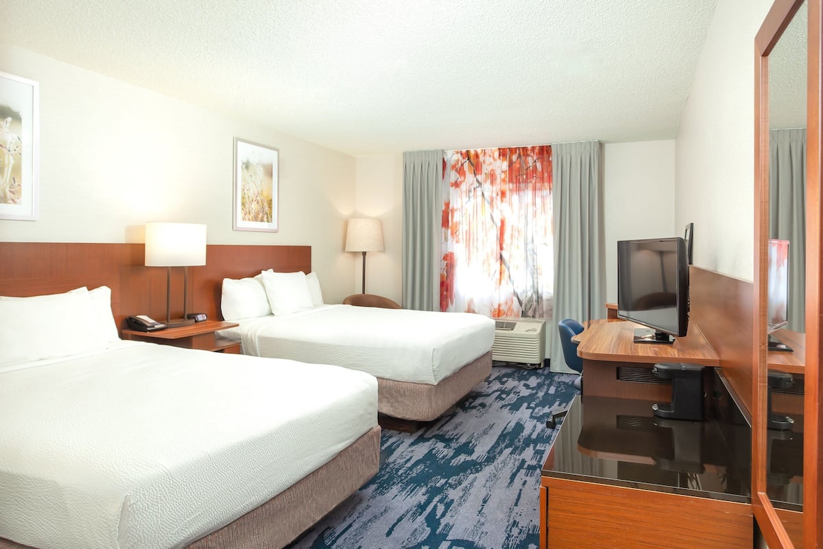 A hotel room with two beds, a desk with a television, a desk lamp, and a window with curtains.