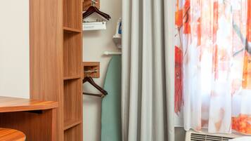 Quarto de hotel com guarda-roupa de madeira, uma cadeira verde e cortina estampada com flores.