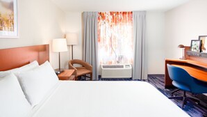 A hotel room with a bed, a desk, a chair, a lamp, and a window with curtains.