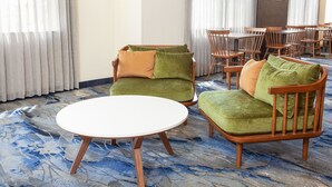 A hotel room with a round white table, two green armchairs with orange cushions, and a wooden chair. - Fairfield inn by Marriott North Little Rock (North Little Rock)