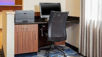 A hotel room with a wooden desk, a computer, and a chair.