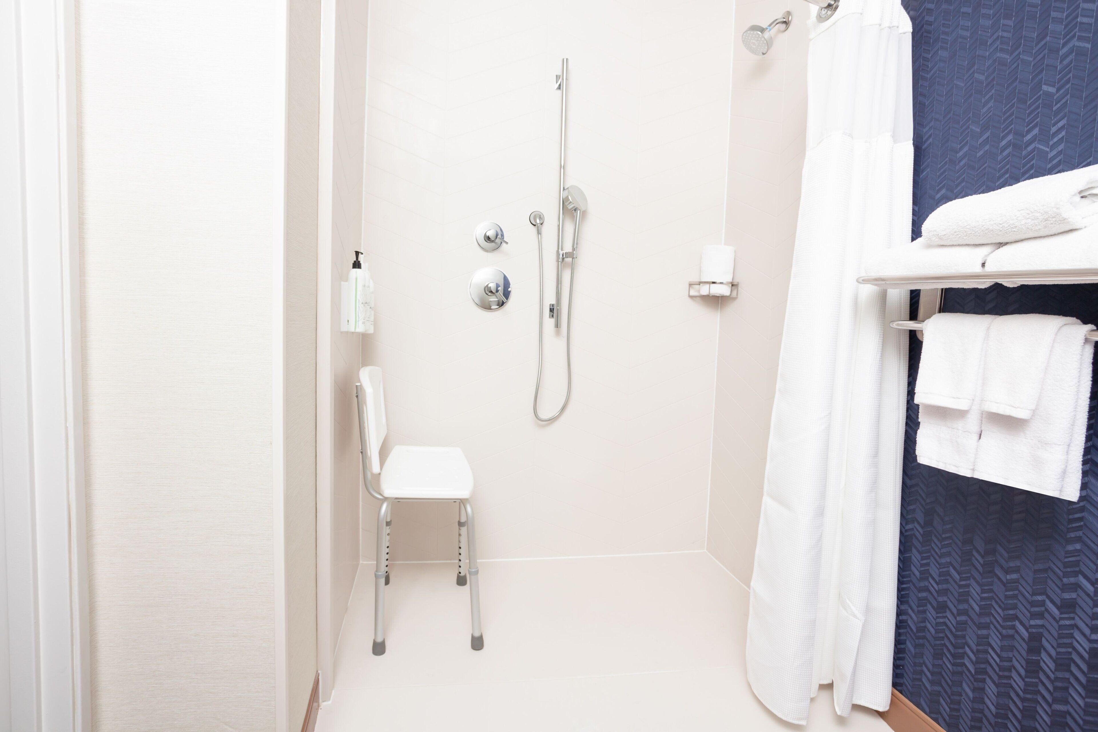 Een moderne badkamer met een douche, een witte stoel en een handdoekhouder.