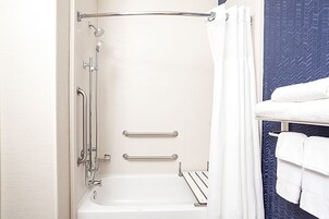 Un baño con bañera, ducha y barras de apoyo.