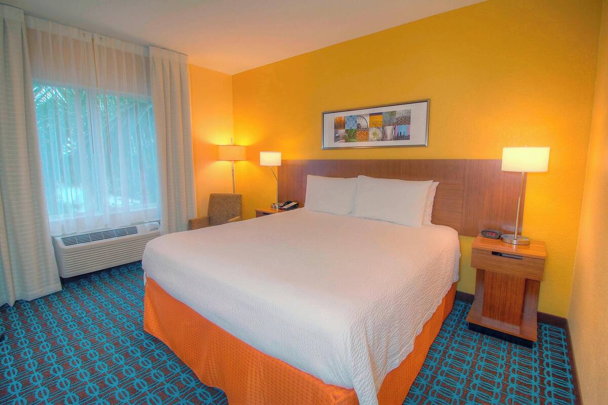 Una habitación de hotel con una cama grande, dos lámparas de noche, una ventana con cortinas y un cuadro colgado en la pared.
