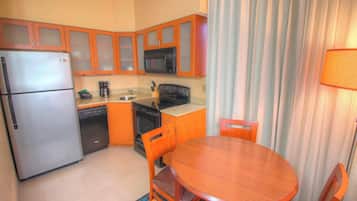 Cocina compacta con refrigerador, microondas, estufa, lavavajillas y armarios de madera.