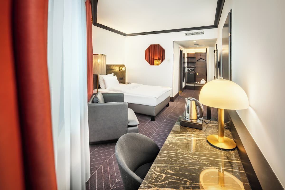 A hotel room with a bed, a desk with a lamp, a chair, and a view of the bathroom.