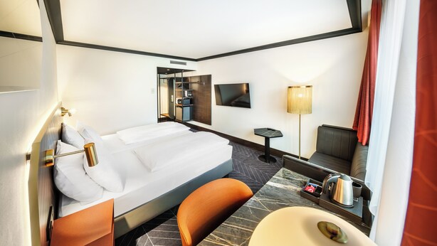 Habitación de hotel con cama, escritorio, silla, televisor, lámpara y baño.