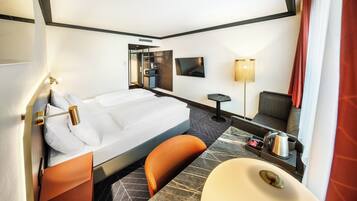 A hotel room with a bed, a desk, a chair, a TV, a lamp, and a bathroom.