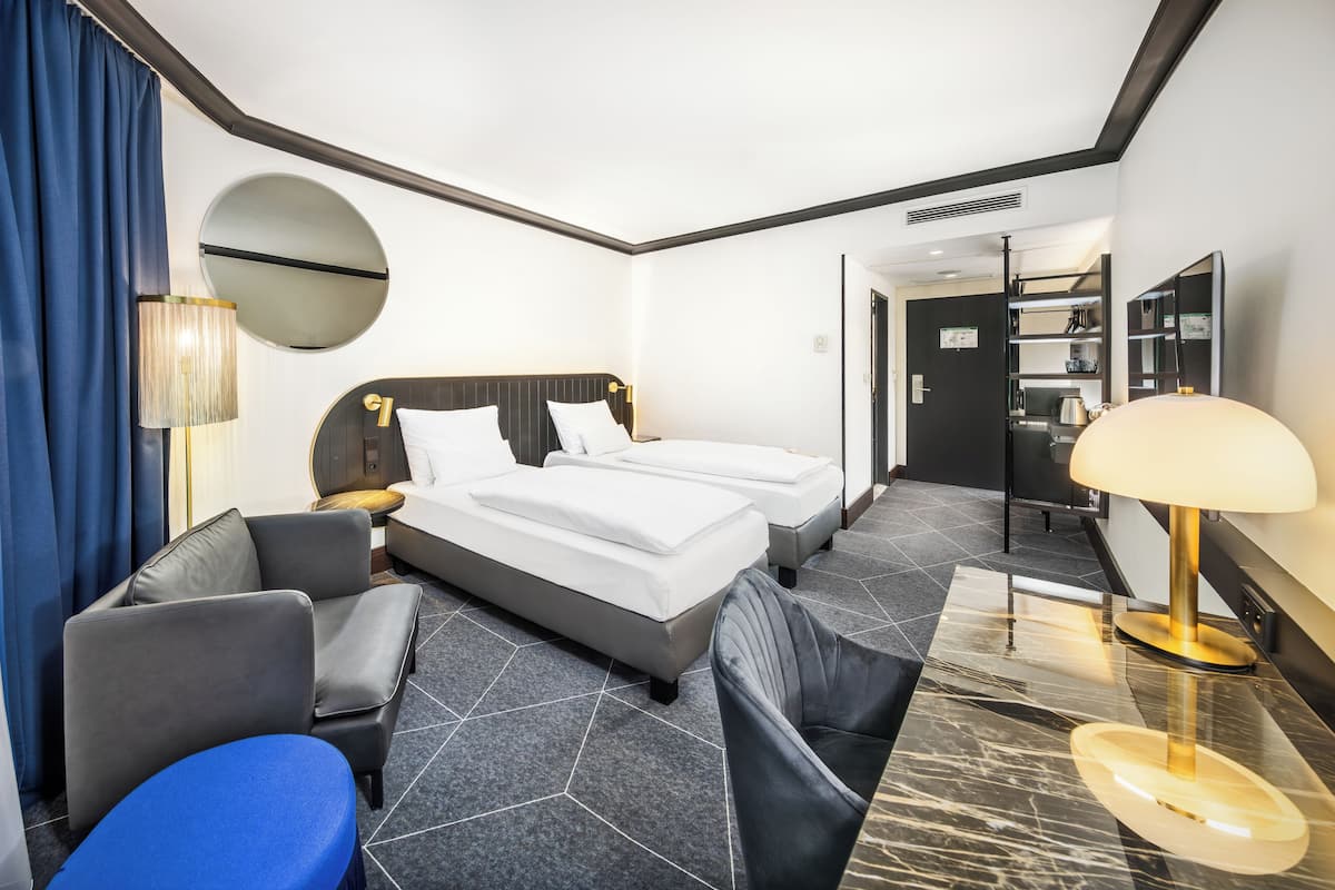 A hotel room with a bed, two bedside tables, a lamp, a chair, a sofa, and a mirror.