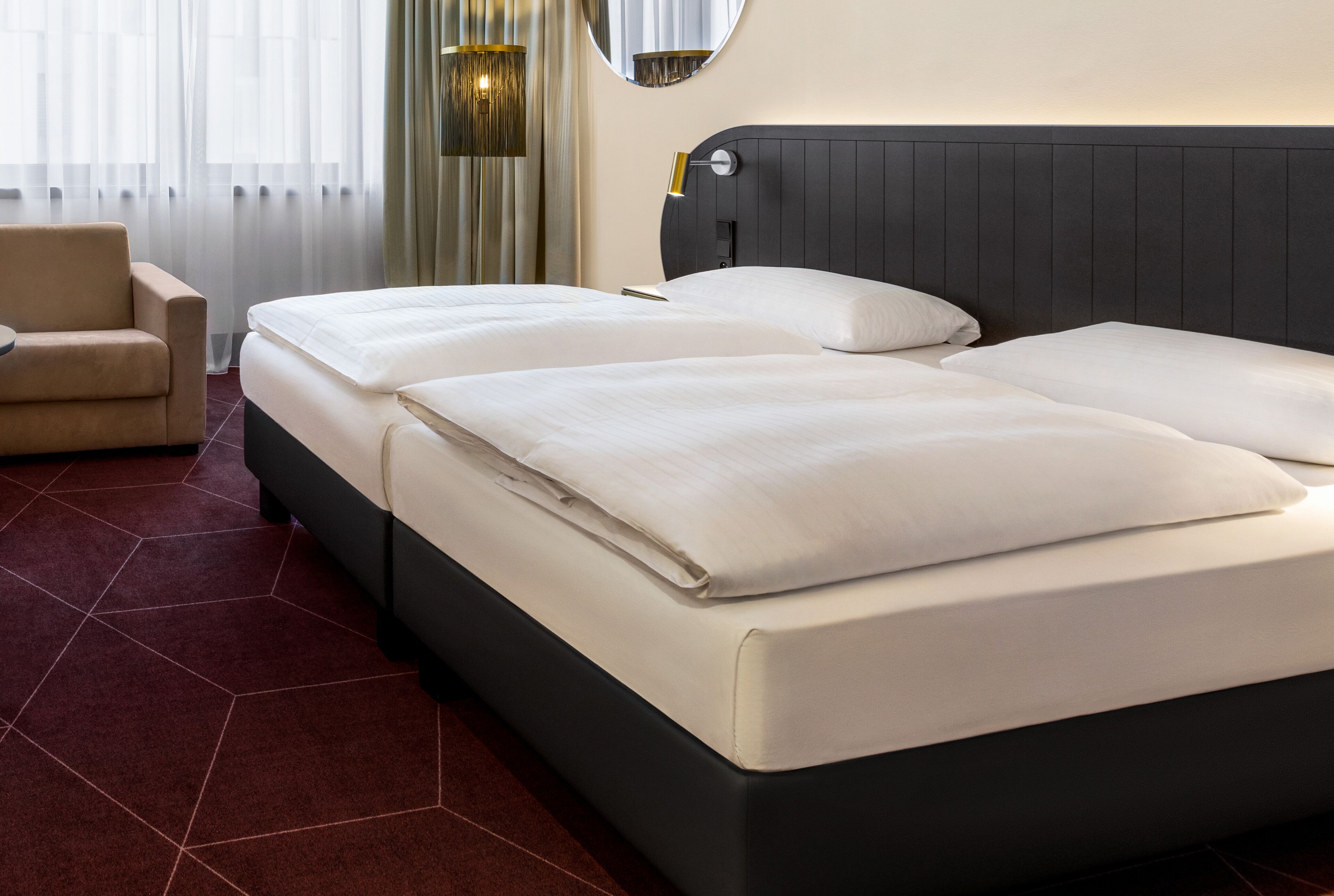 A hotel room with two beds, a chair, and a large mirror.