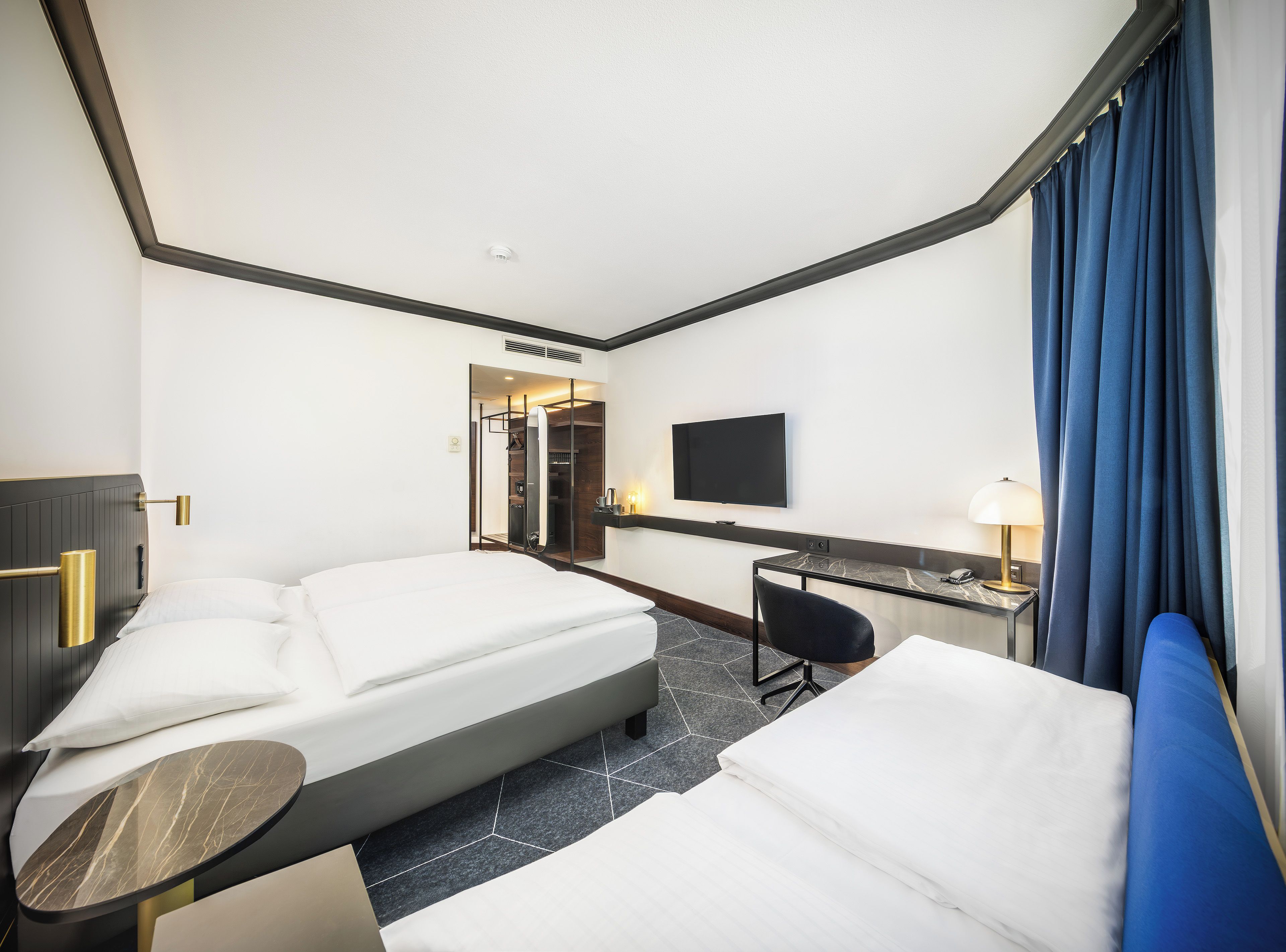 A hotel room with a bed, a desk, a chair, a TV, and a bathroom visible through a door.