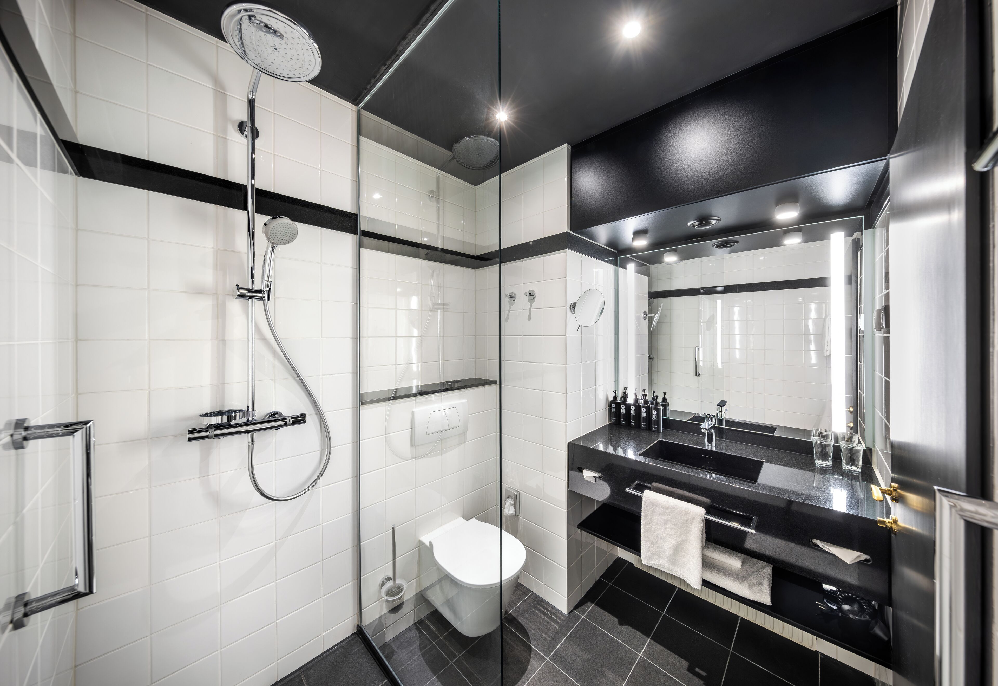 A modern bathroom with a glass-enclosed shower, a white toilet, and a black vanity with a large mirror.