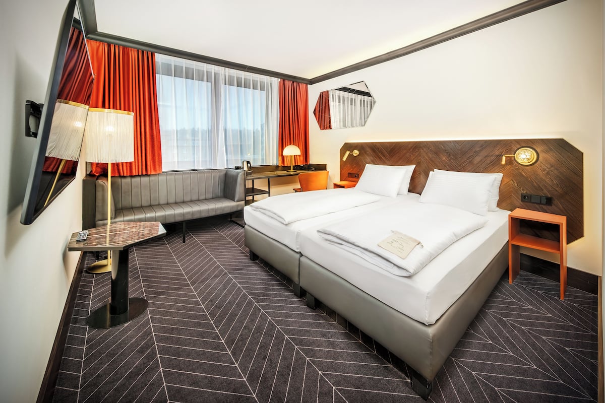 A hotel room with a large bed, a sofa, a desk, and a mirror.