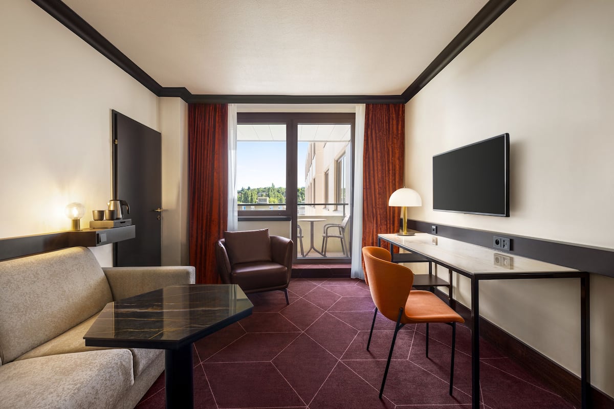 A hotel room with a sofa, a dining table, a TV, and a balcony with a view.